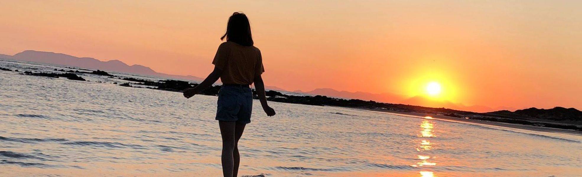Junge Frau am Strand bei Sonnenuntergang – Unsere FAQs zur Freiwilligenarbeit im Ausland