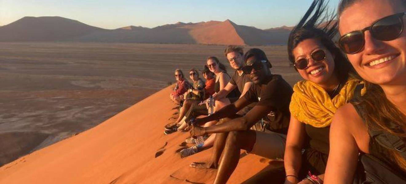 Travelers sit smiling on Dune 45 in Namibia